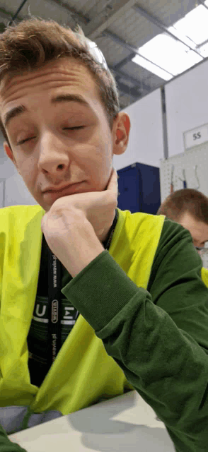 a man wearing a green shirt and a yellow vest has a lanyard around his neck that says ss