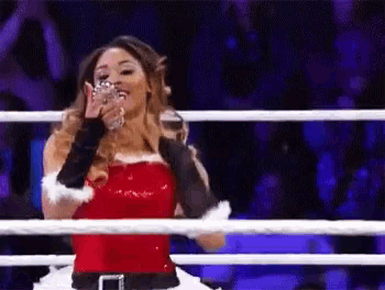 a woman in a santa claus costume is standing in a boxing ring holding a glass .