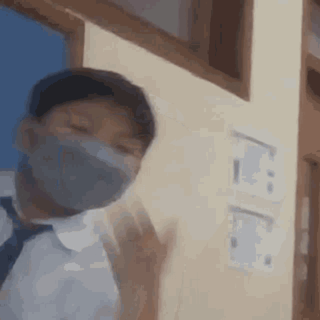 a young boy wearing a mask and a tie is standing in a classroom .