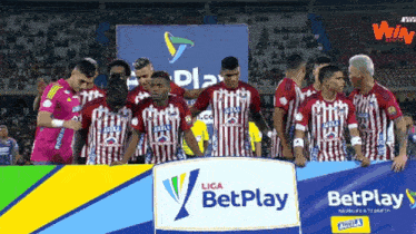 a group of soccer players are standing in front of a betplay sign