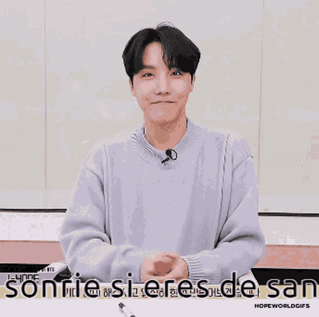a man in a grey sweater is smiling and making a heart with his fingers