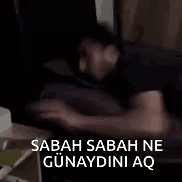 a man is laying on a bed with the words sabah sabah ne günaydini aq written above him .