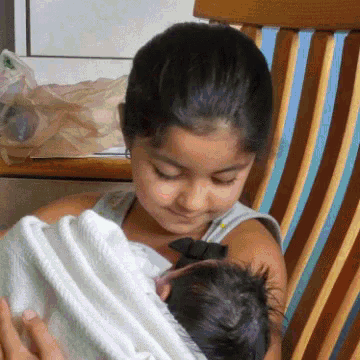 a young girl is holding a baby in her lap