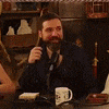 a man with a beard is sitting at a table with a microphone in front of him .