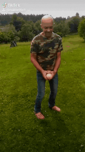 a man in a camouflage shirt is standing in the grass holding a ball in his hands .