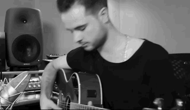 a man in a black shirt is playing an acoustic guitar in front of two speakers
