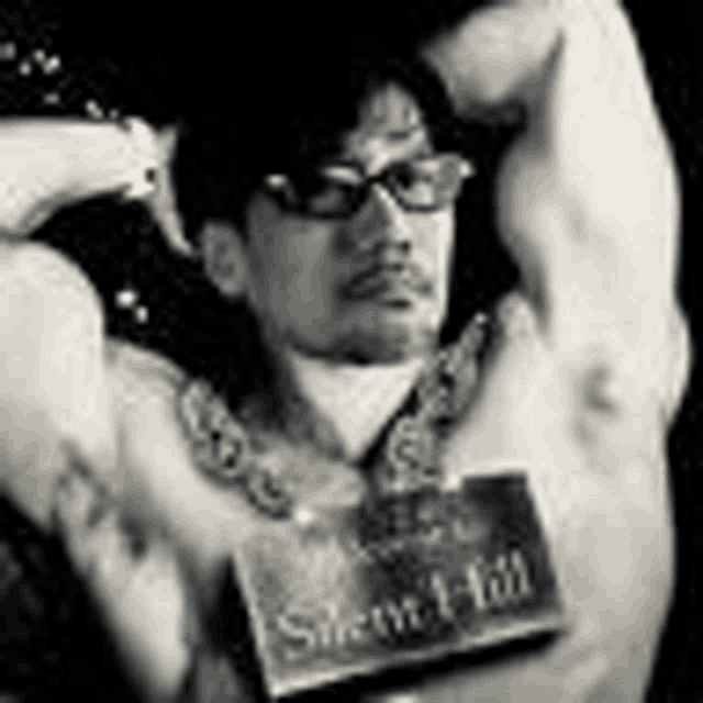 a black and white photo of a shirtless man wearing glasses and holding a book .