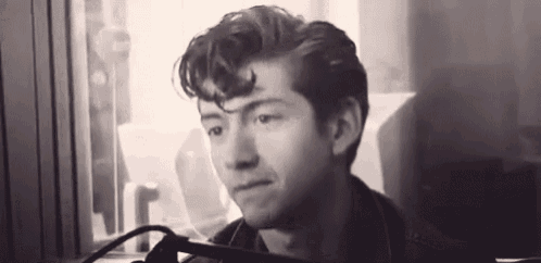 a black and white photo of a man sitting in front of a microphone in a room .