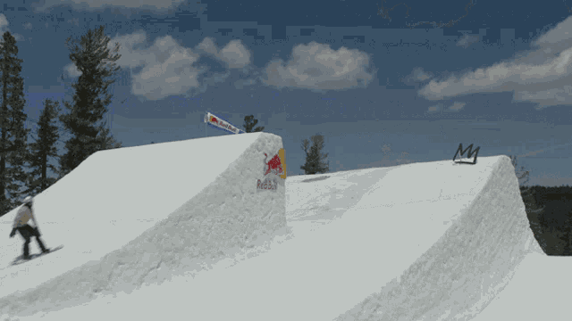 a snowboarder is going down a snowy ramp with a red bull banner hanging from the side
