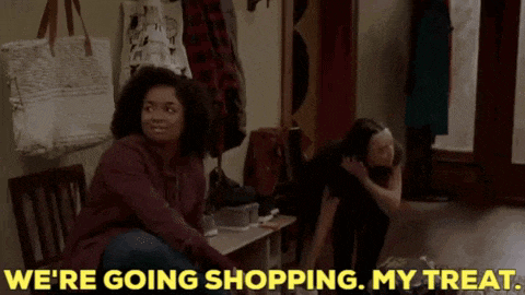 a woman is sitting on a bench in a hallway talking to another woman who is standing next to her .