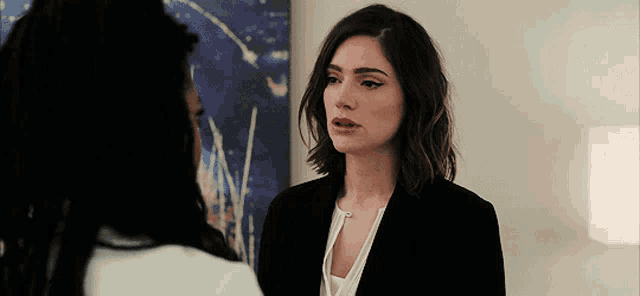a woman in a black suit is talking to another woman in front of a painting