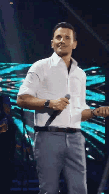 a man in a white shirt and grey pants is singing into a microphone