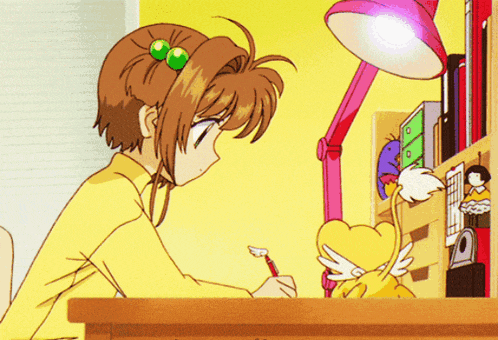 a girl in a yellow shirt sits at a desk with a cat