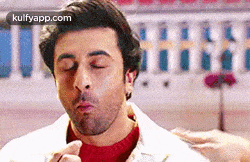 a man is blowing a kiss with his eyes closed in front of a building .