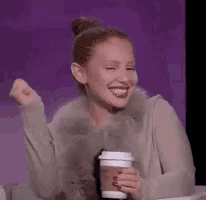 a woman is sitting at a table holding a cup of coffee and laughing .