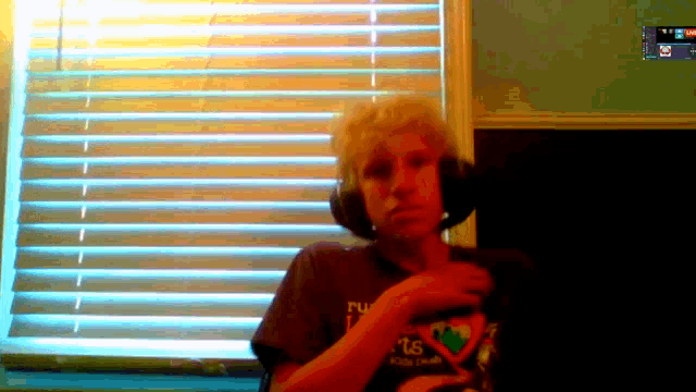 a man wearing headphones and a shirt that says ' rv ' on it stands in front of a window
