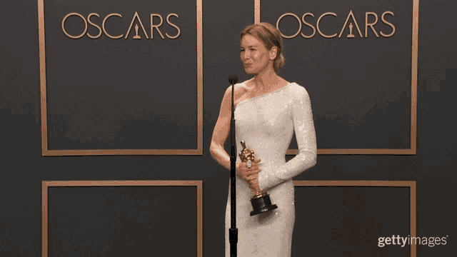 a woman in a white dress is holding an oscar