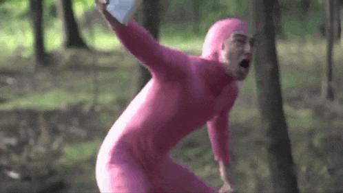 a man in a pink suit is standing in the woods holding a piece of paper .