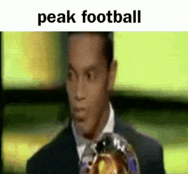 a man in a suit is holding a soccer ball and the words peak football are on the bottom