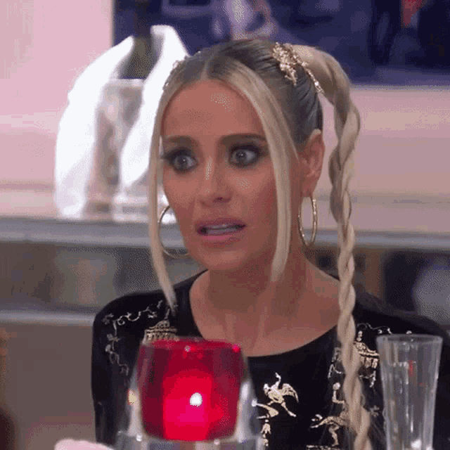 a woman in a braided ponytail is sitting at a table with a red candle in front of her .