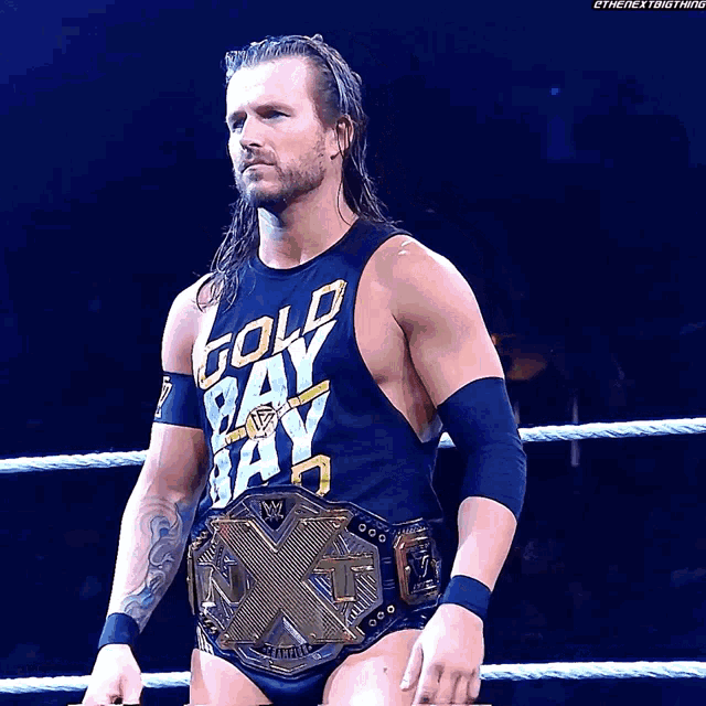a wrestler wearing a gold bay bay shirt stands in the ring