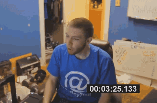 a man wearing a blue shirt with the letter a on it sits in front of a computer