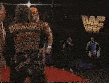 a man in a blue tank top is kicking another man in a yellow shorts in a wrestling match .