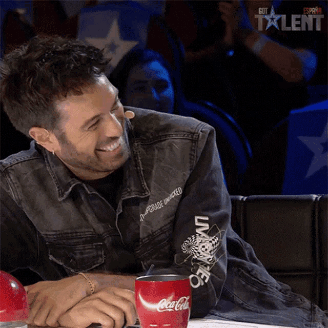 a man in a denim jacket sits next to a coca cola cup
