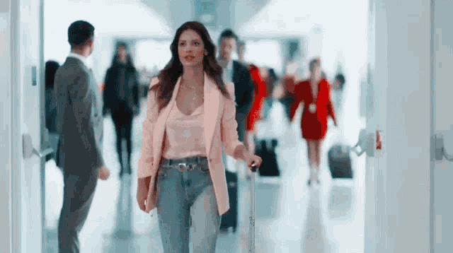 a woman in a pink jacket is walking down a hallway carrying a suitcase