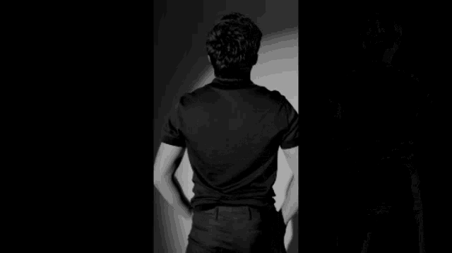 a man in a black shirt is standing in front of a white wall