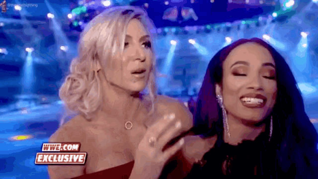 two women are standing next to each other on a stage with a sign that says wwe.com exclusive on it .