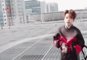 a young man in a red and black sweater is standing on a rooftop looking at his watch .