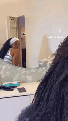 a woman with curly hair is looking at herself in a mirror .