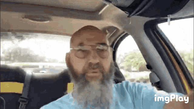 a man with a beard and glasses is sitting in a car with imgplay written on the bottom right