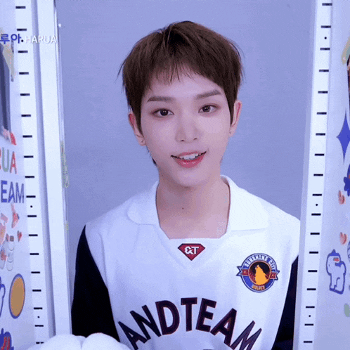 a boy wearing a white and team jersey stands next to a height chart
