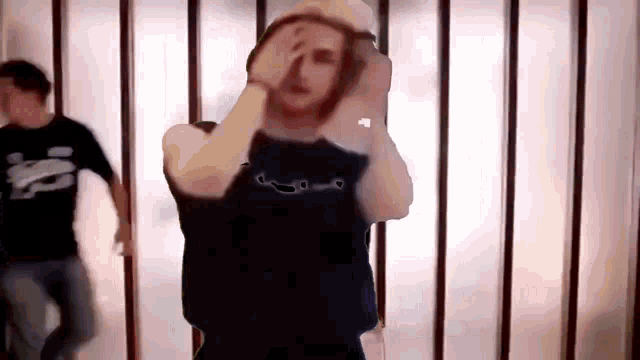 a man in a black shirt is standing in front of a glass wall holding his head .