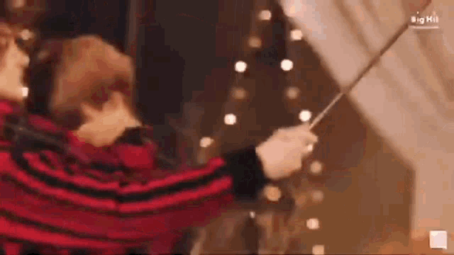 a man in a red and black striped shirt is holding a stick in front of a string of lights .