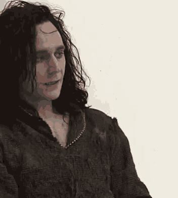 a man with long black hair is wearing a green sweater and looking at the camera .