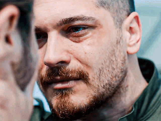 a close up of a man 's face with a beard and a green shirt