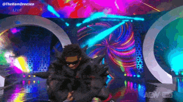 a man in a black costume is dancing on a stage with a colorful background .
