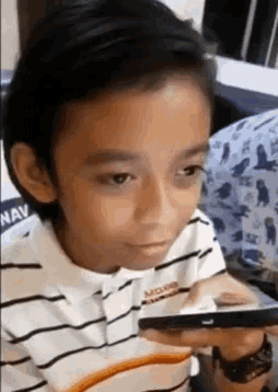 a young boy in a striped shirt is holding a cell phone in his hand .