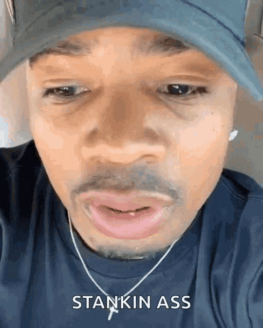 a man wearing a hat and a necklace has the word stankin ass on his face