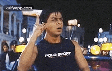 a man wearing a polo sport tank top is making a funny face while holding his hand to his ear .