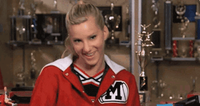 a cheerleader in a red jacket with the letter m on it is smiling .