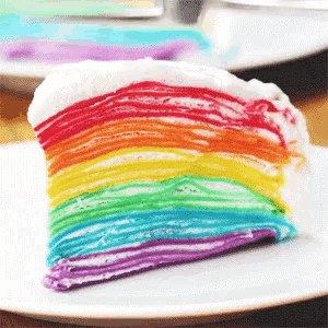 a white plate topped with a slice of rainbow colored cake