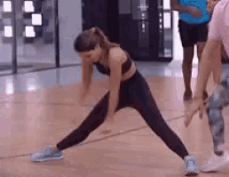 a woman is doing a stretching exercise on a wooden floor in a gym .