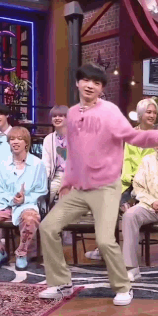 a man in a pink sweater is dancing in front of a group of people sitting on chairs .