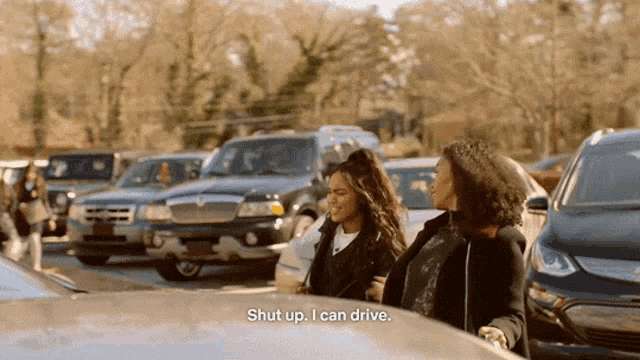 two women are standing in a parking lot talking to each other and one of them says " shut up i can drive "