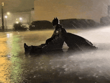a man in a batman costume is laying in the rain