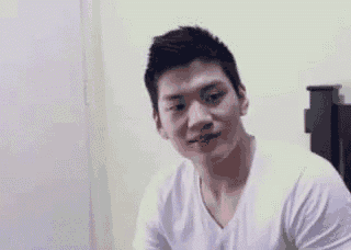 a man in a white shirt is sitting in front of a bed and smiling .